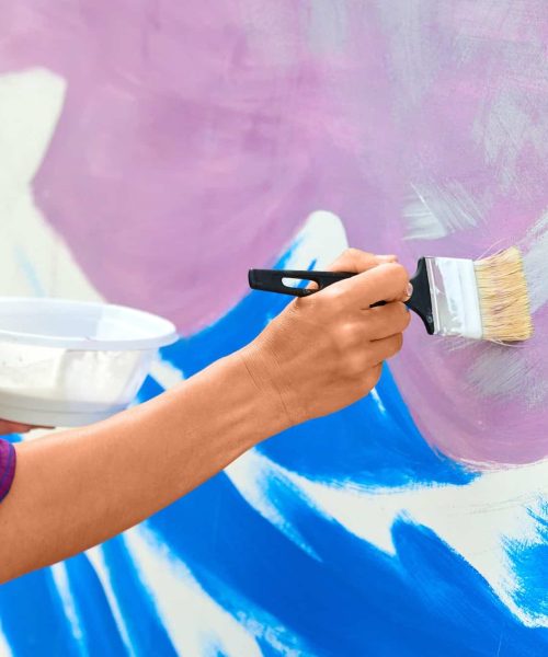 female-artist-working-on-abstract-acrylic-painting-hand-holding-paint-brush-large-canvas-outdoor.jpg